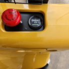 Close-up of a yellow industrial control panel featuring a large red emergency stop button on the left and a circular gauge on the right.