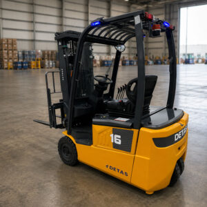 Yellow forklift in a spacious warehouse, cockpit visible with steering wheel and control levers, labeled '16' and 'DETAS' on the side.