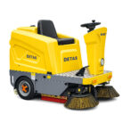 Yellow street-sweeping vehicle with two large brush heads in front and a black seat, labeled DETAS on the side and front plate.