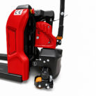 Close-up of a red and black pallet jack/electric stacker with a front wheel and control handle visible.