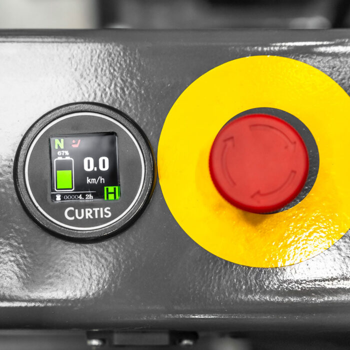 Curtis control panel with a digital display showing 0.0 km/h and a red emergency stop button with a yellow surround.