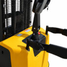 Close-up of a yellow forklift showing the steering column, black control levers, and a key in the ignition with a metal mesh guard in the background.